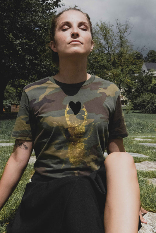 Golden scarab with black plush heart on a military pattern tee